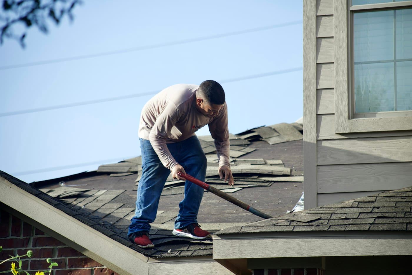 A roofer removing worn asphalt shingles from a pitched roof